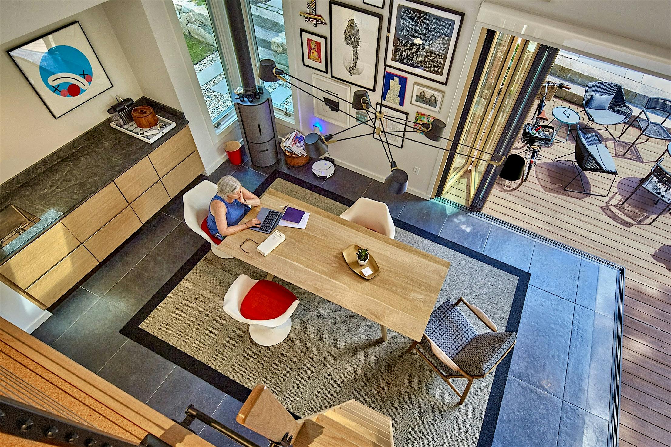 Modern art studio features large windows, light wooden cabinets, and cornerless bi-folding doors that open to an adjacent outdoor patio with seating.
