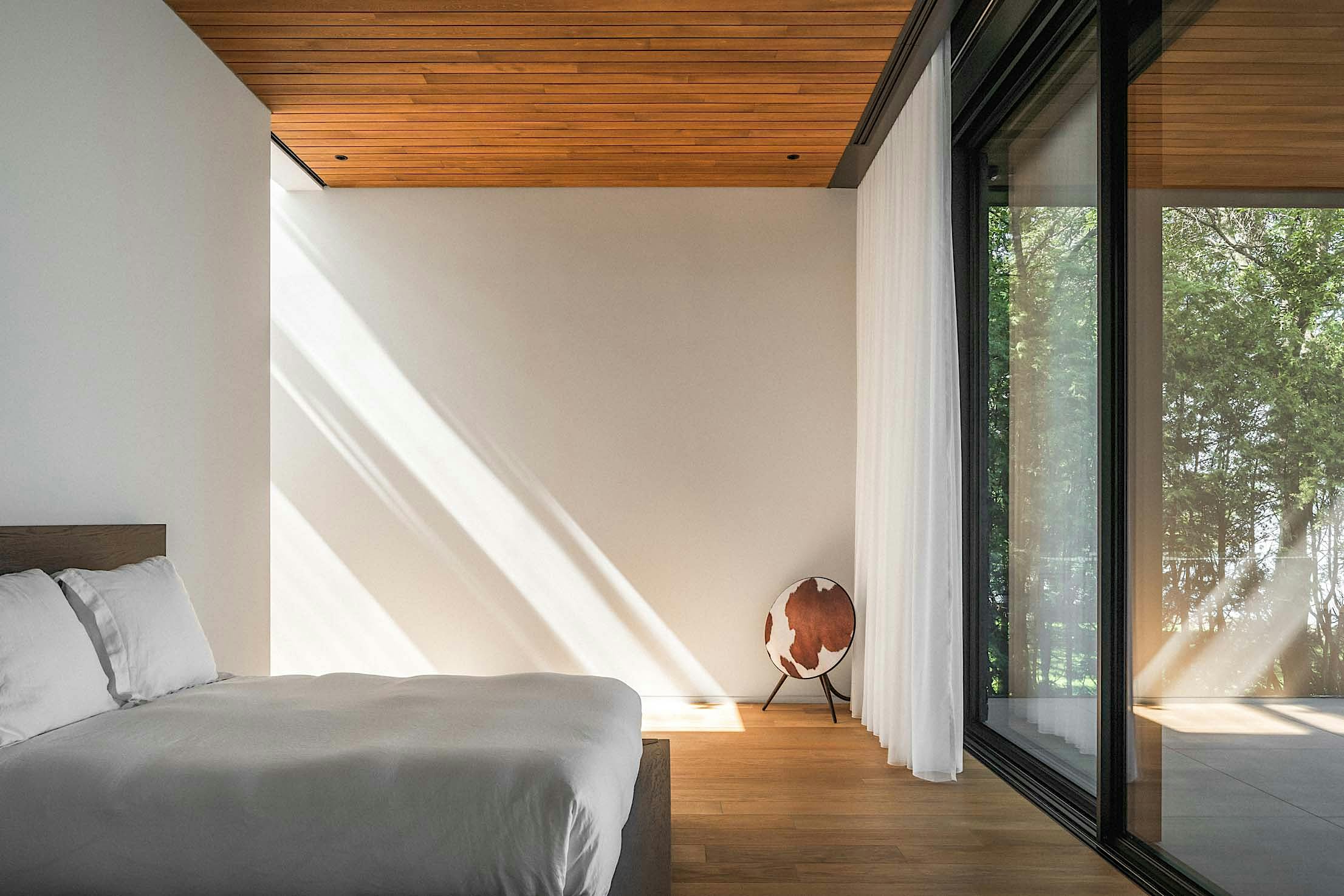 Minimalist bedroom with a wooden ceiling, large window, white bed, and globe decoration.