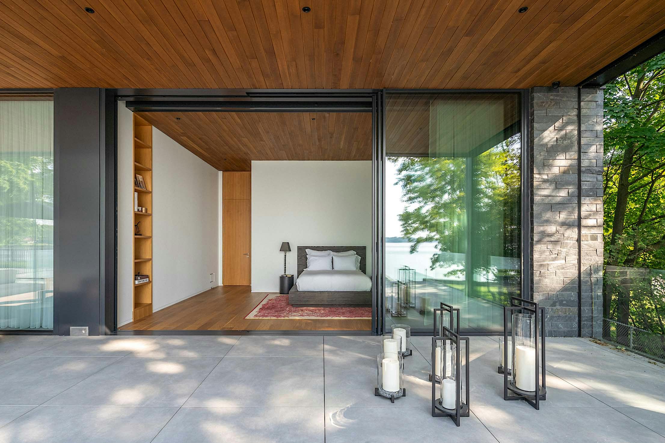 A modern bedroom with glass walls opens to a concrete patio.