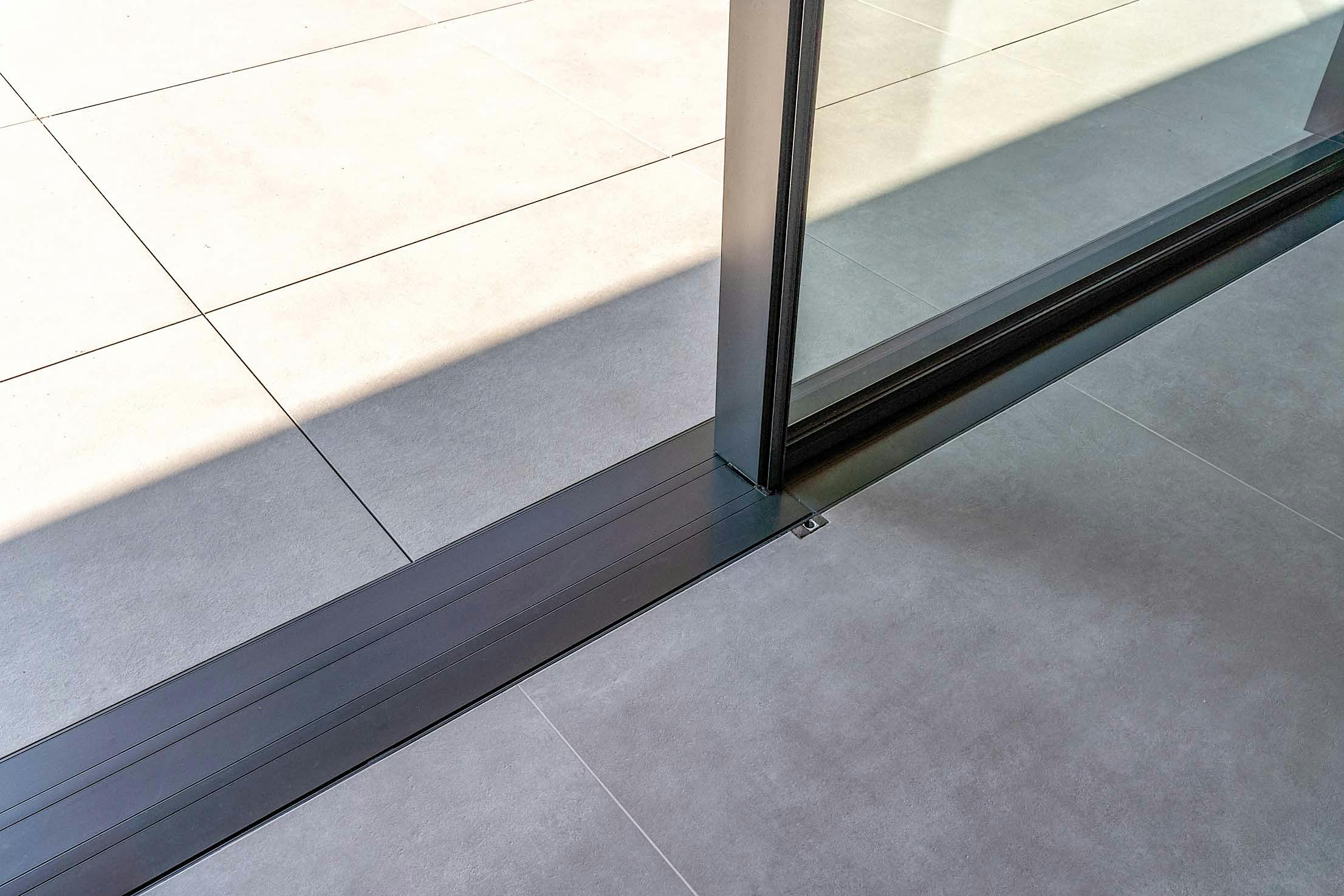 Close-up of a cero sliding glass door partially open, showcasing the sleek metal track along the floor.