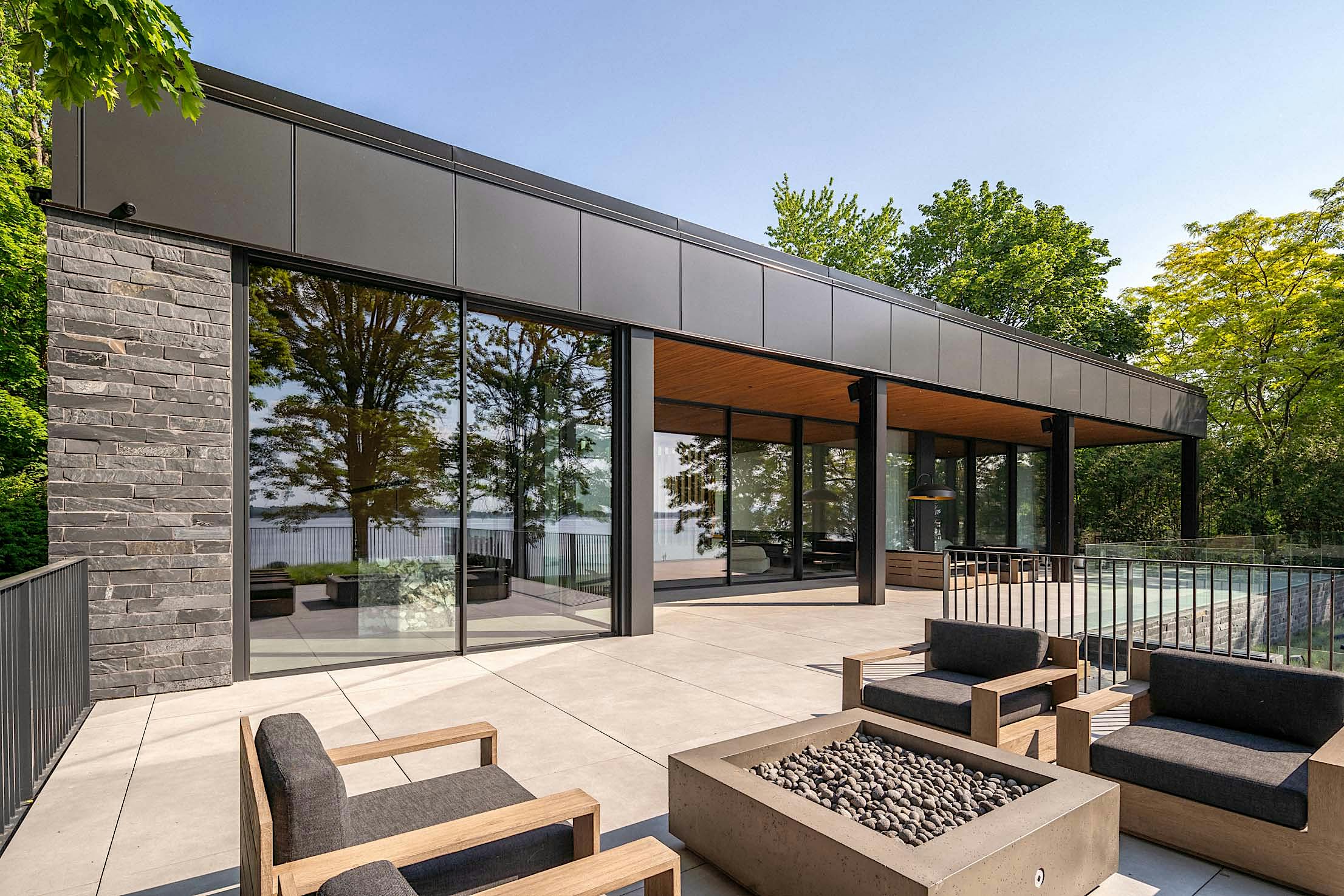 Modern house with large glass doors, a spacious patio featuring outdoor furniture, and a fire pit.