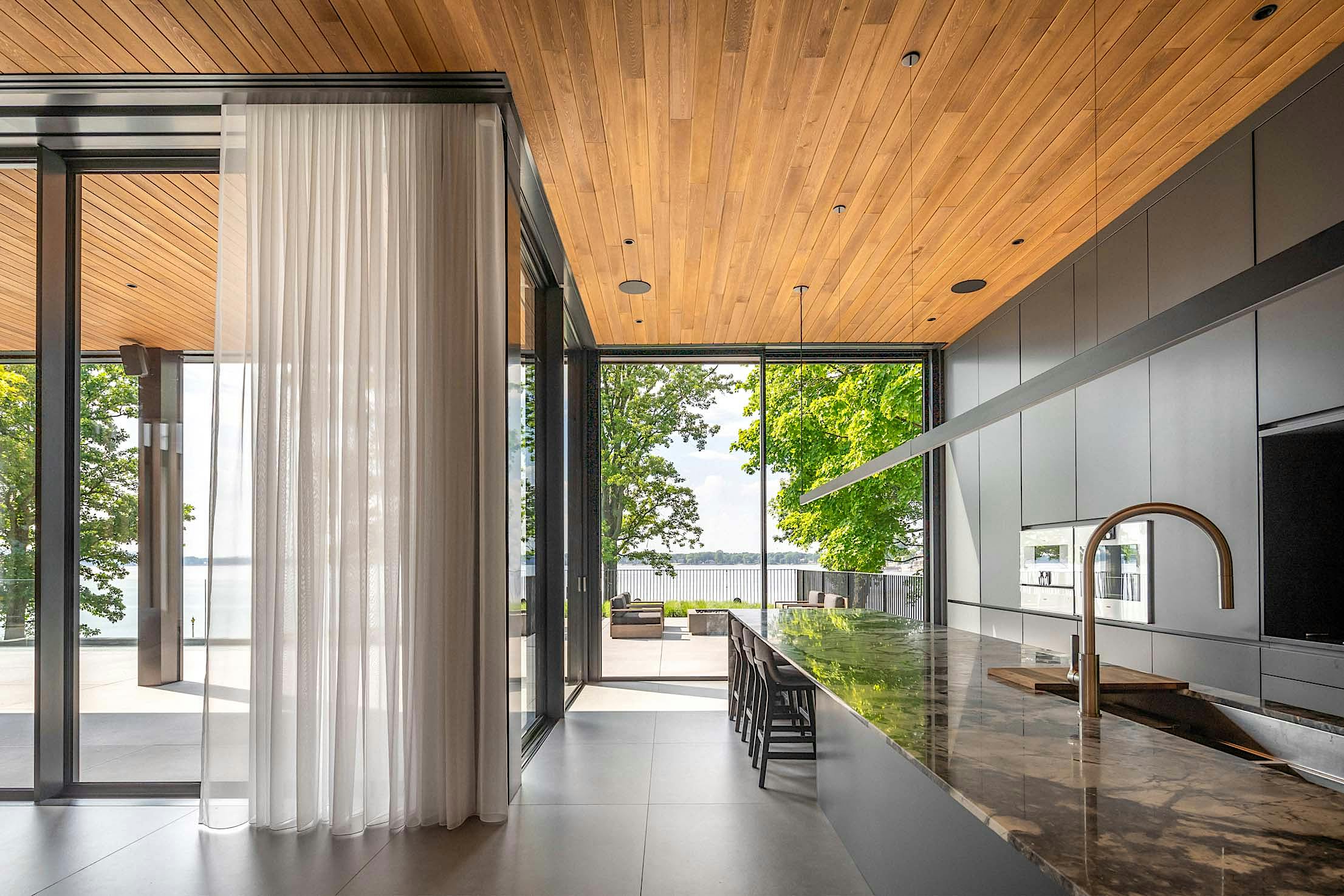 Modern kitchen with a marble island, sleek cabinetry, and large glass doors offering a view of a patio and water beyond.