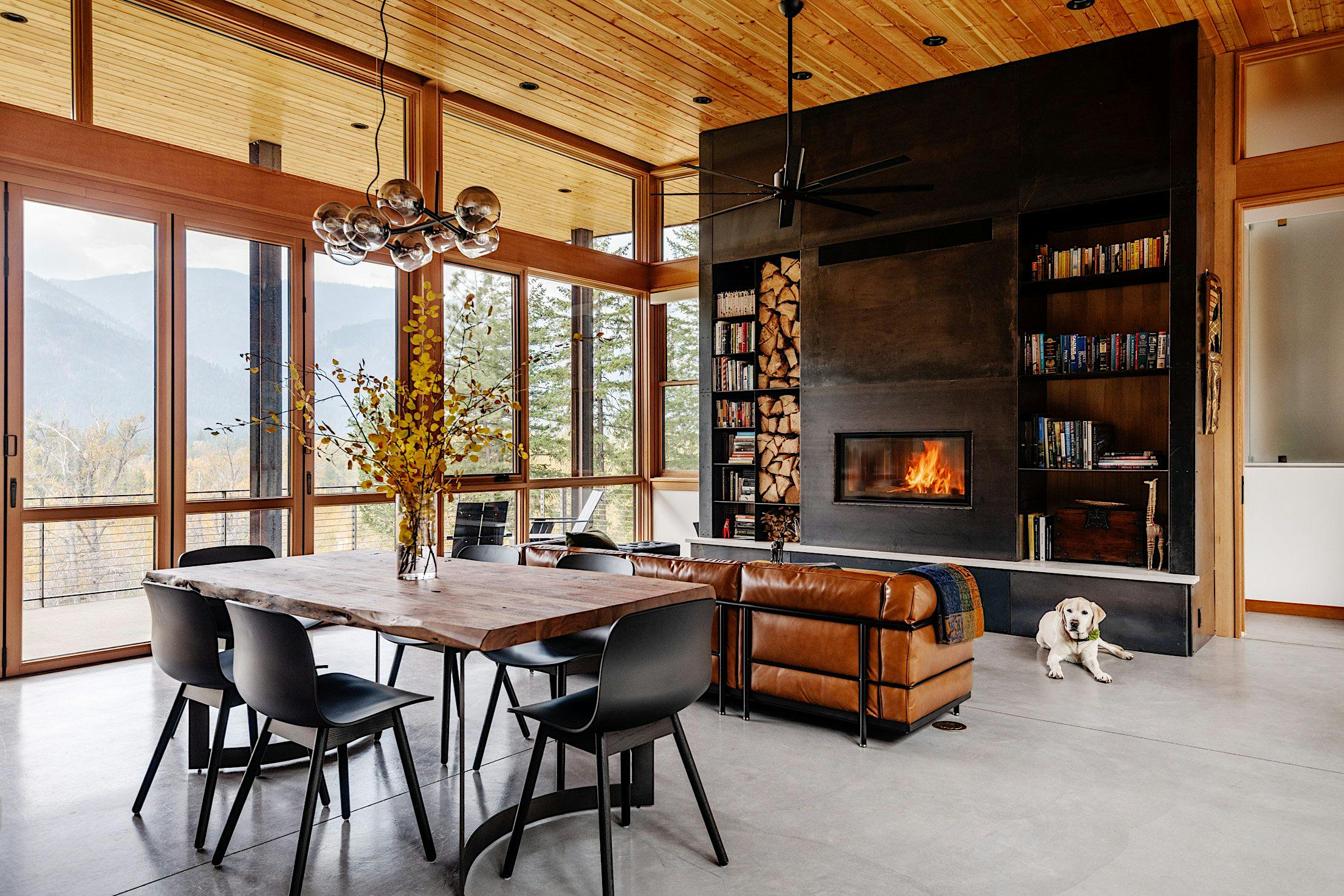 Modern living room with large folding windows, wooden ceiling, and concrete floor.