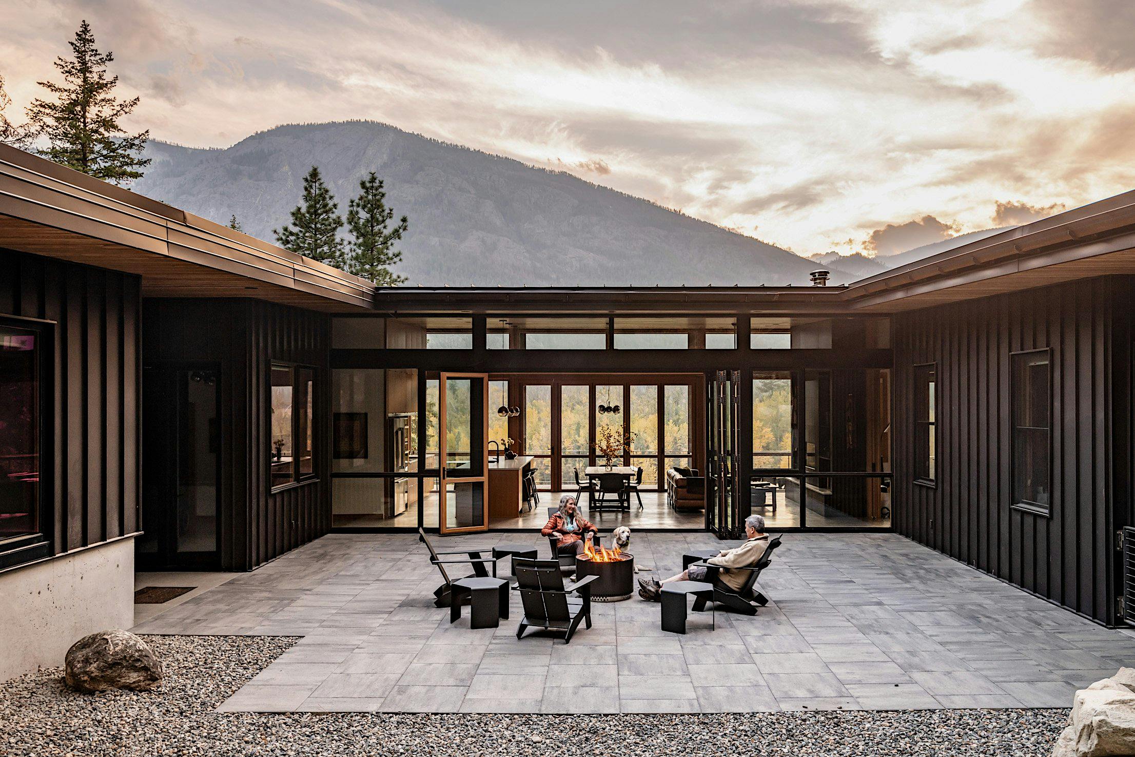 Modern house courtyard with folding glass doors leading to an outdoor seating area, surrounded by a mountainous landscape.