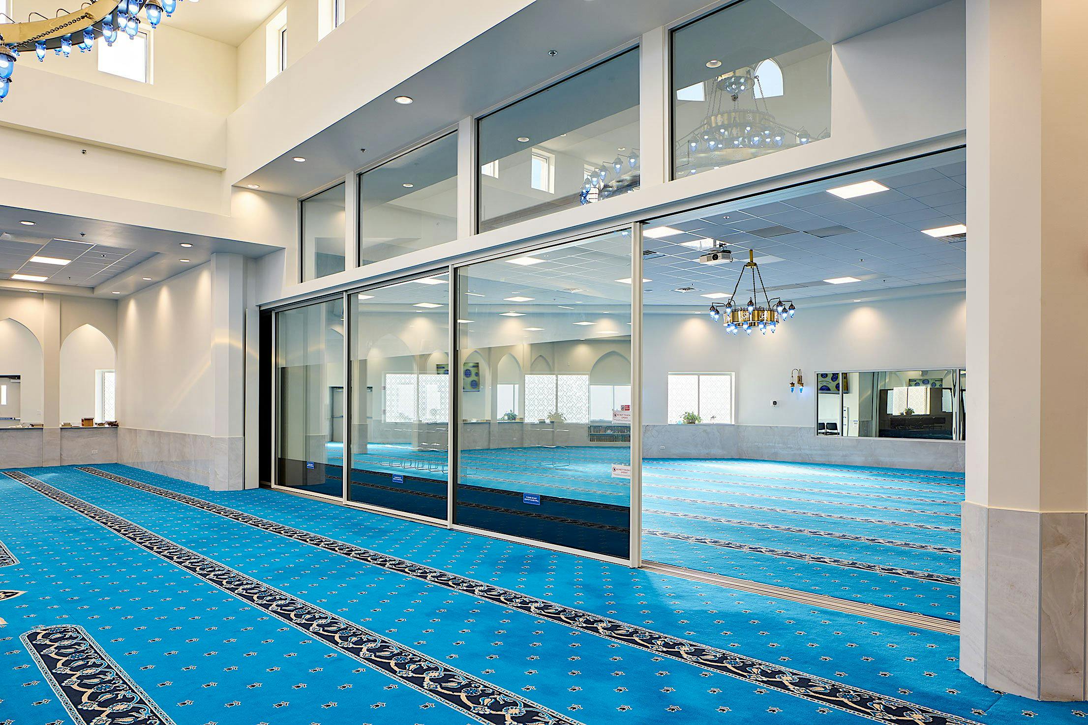 The interior of the mosque features large sliding glass doors with transoms that open up to invite natural light.