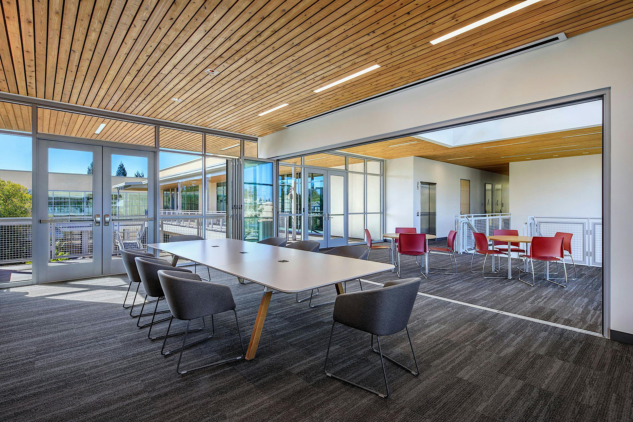 Modern classroom space with glass partition walls and long conference table with black chairs.