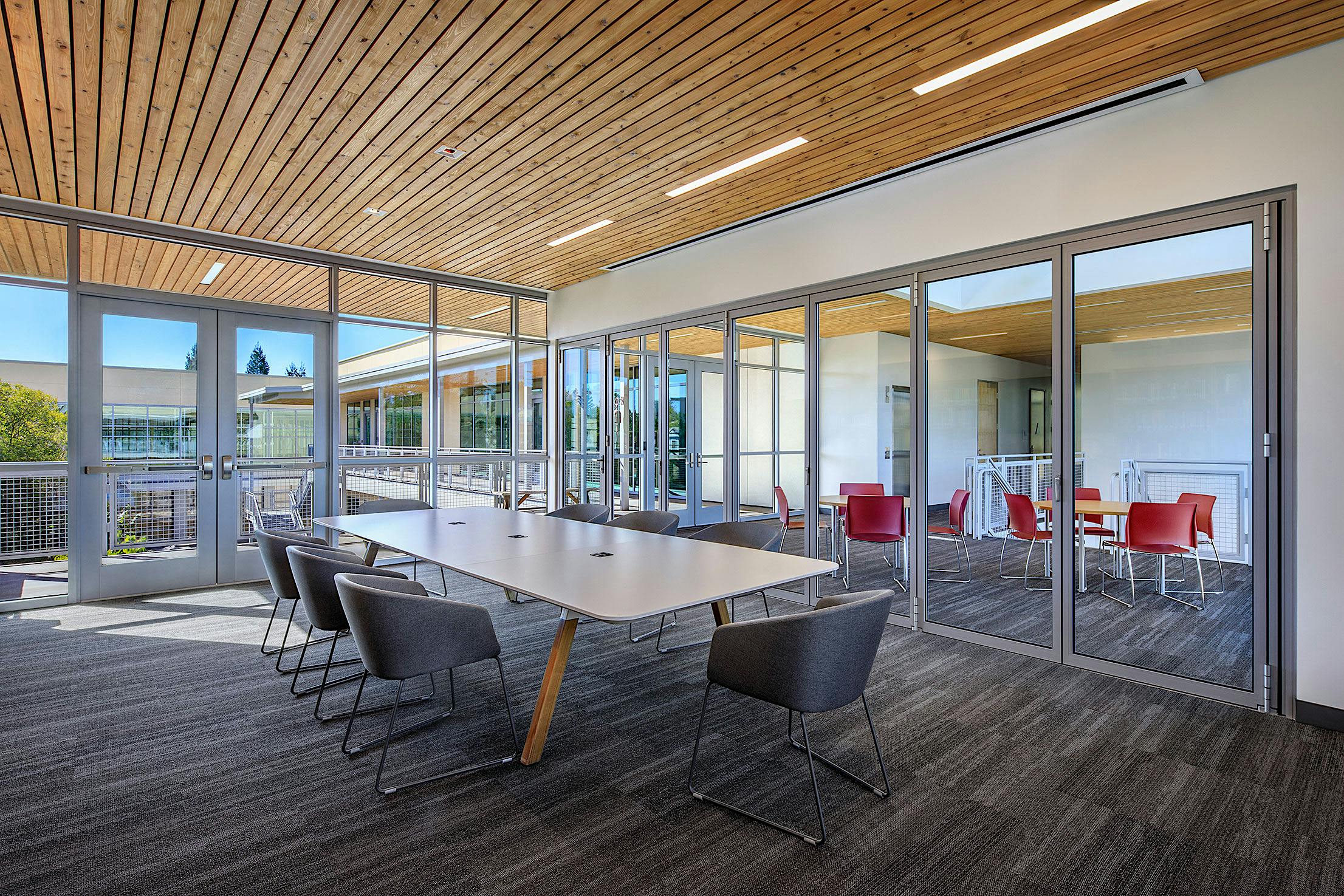 Modern classroom space with glass partition walls and long conference table with black chairs.