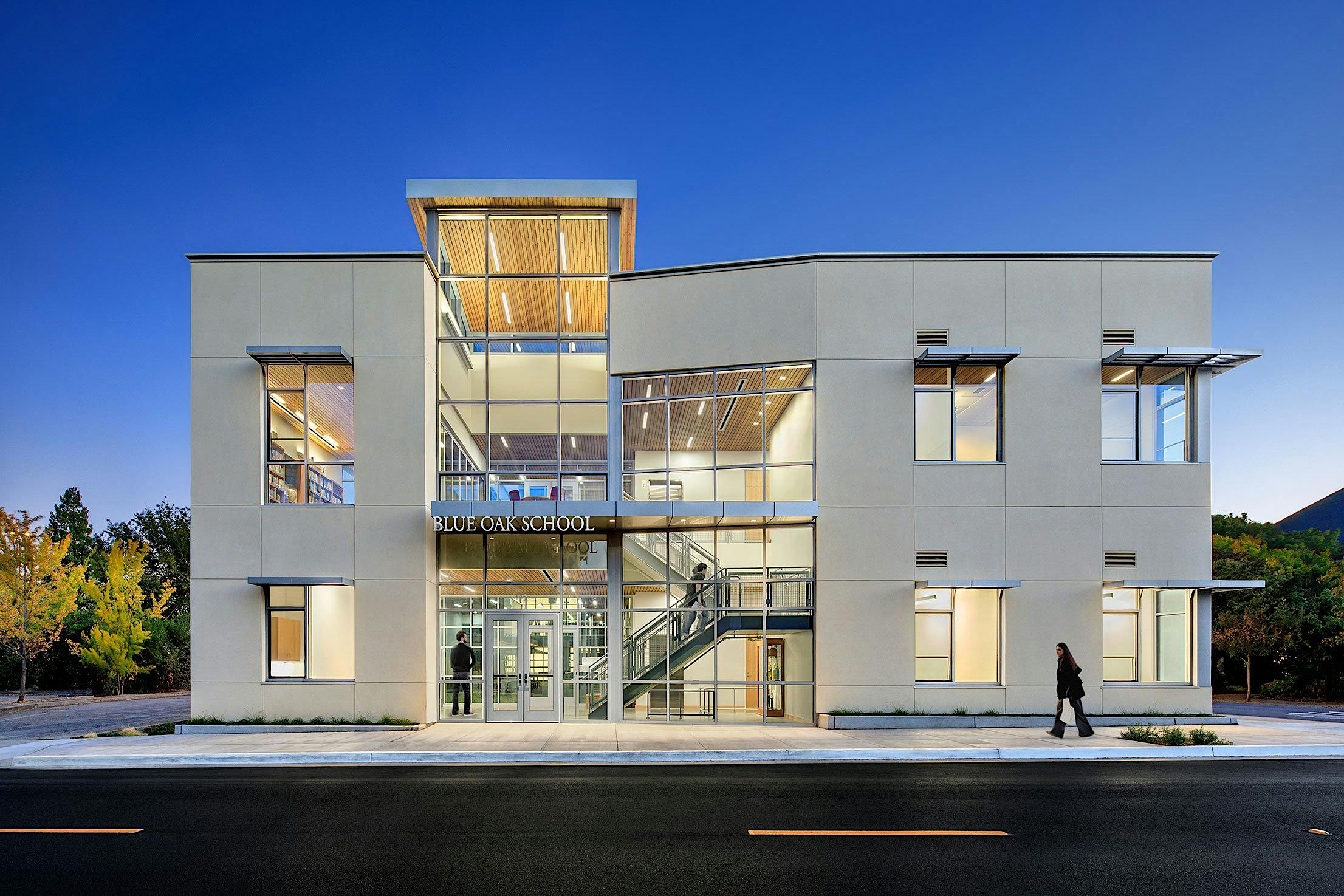 Two-story modern school building with large windows and a central entrance with bifold glass doors.