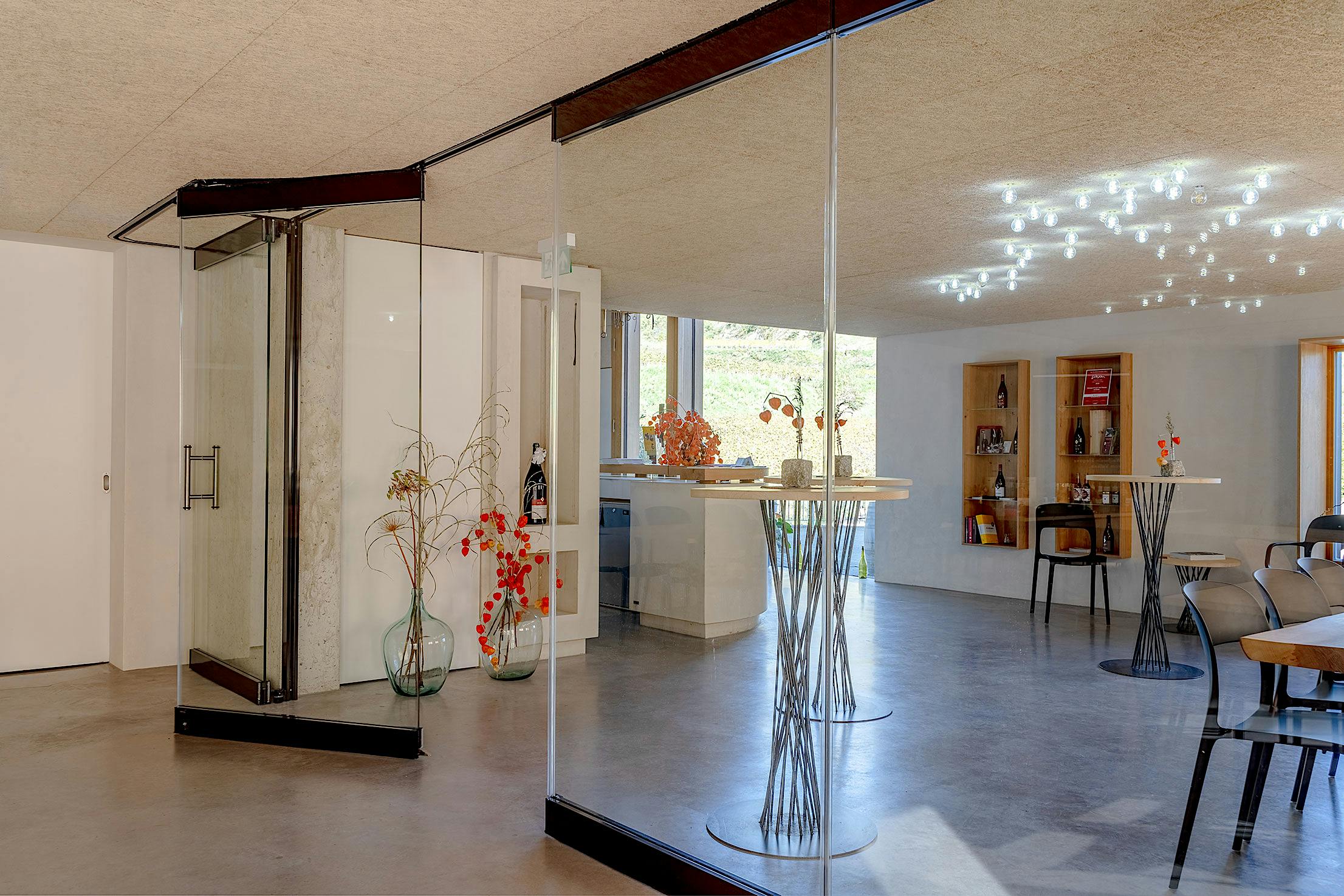 Modern wine tasting interior with partially open glass walls, decorative plants, and a bar area.