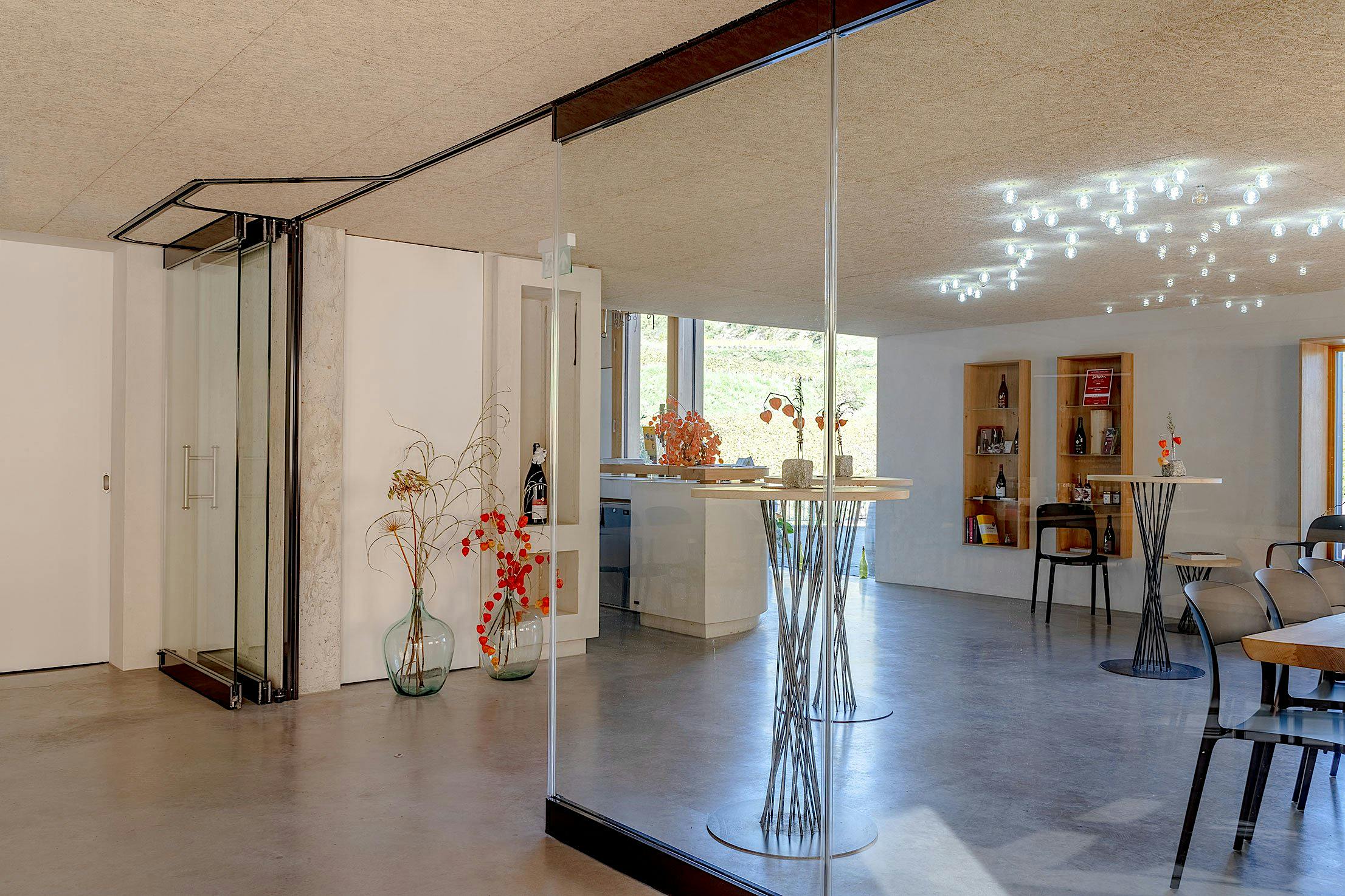 Modern wine tasting room interior with glass partition walls, tall tables, and ceiling lights.