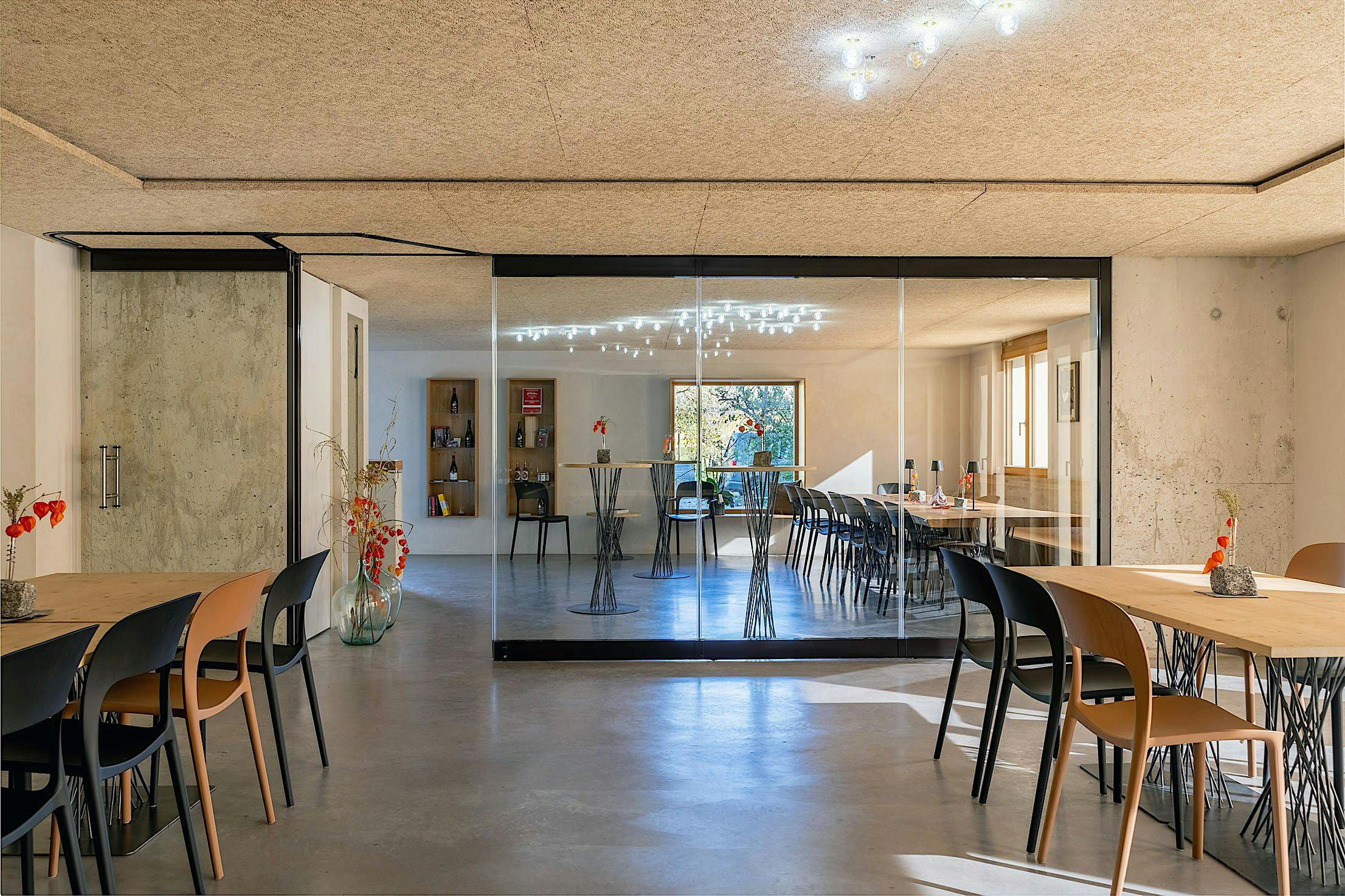 A modern wine tasting area. Decorative vases with red flowers grace the tables, while natural light streams in through large sliding glass doors