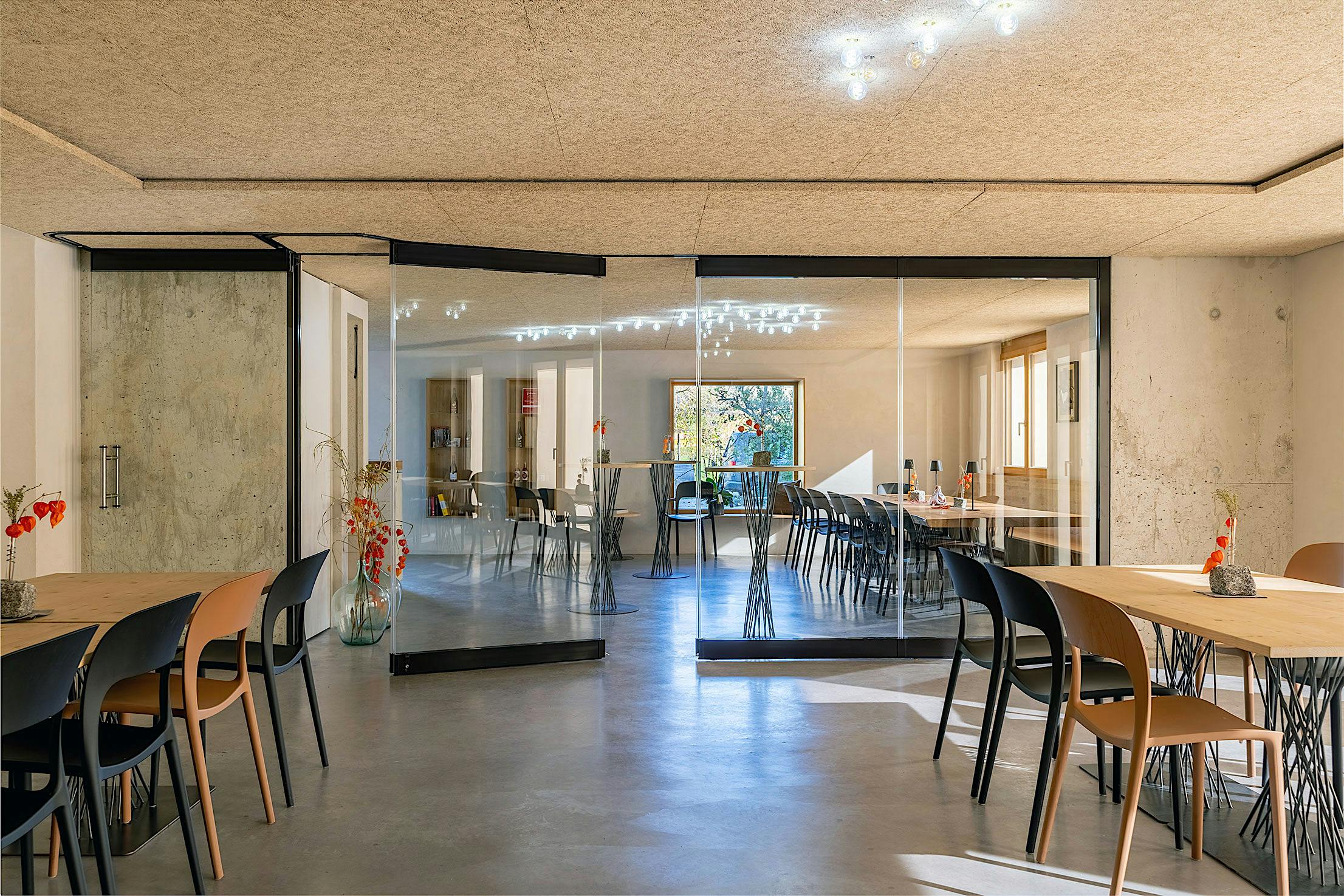 Modern wine tasting area featuring partially open sliding glass doors, wooden tables, and black chairs.