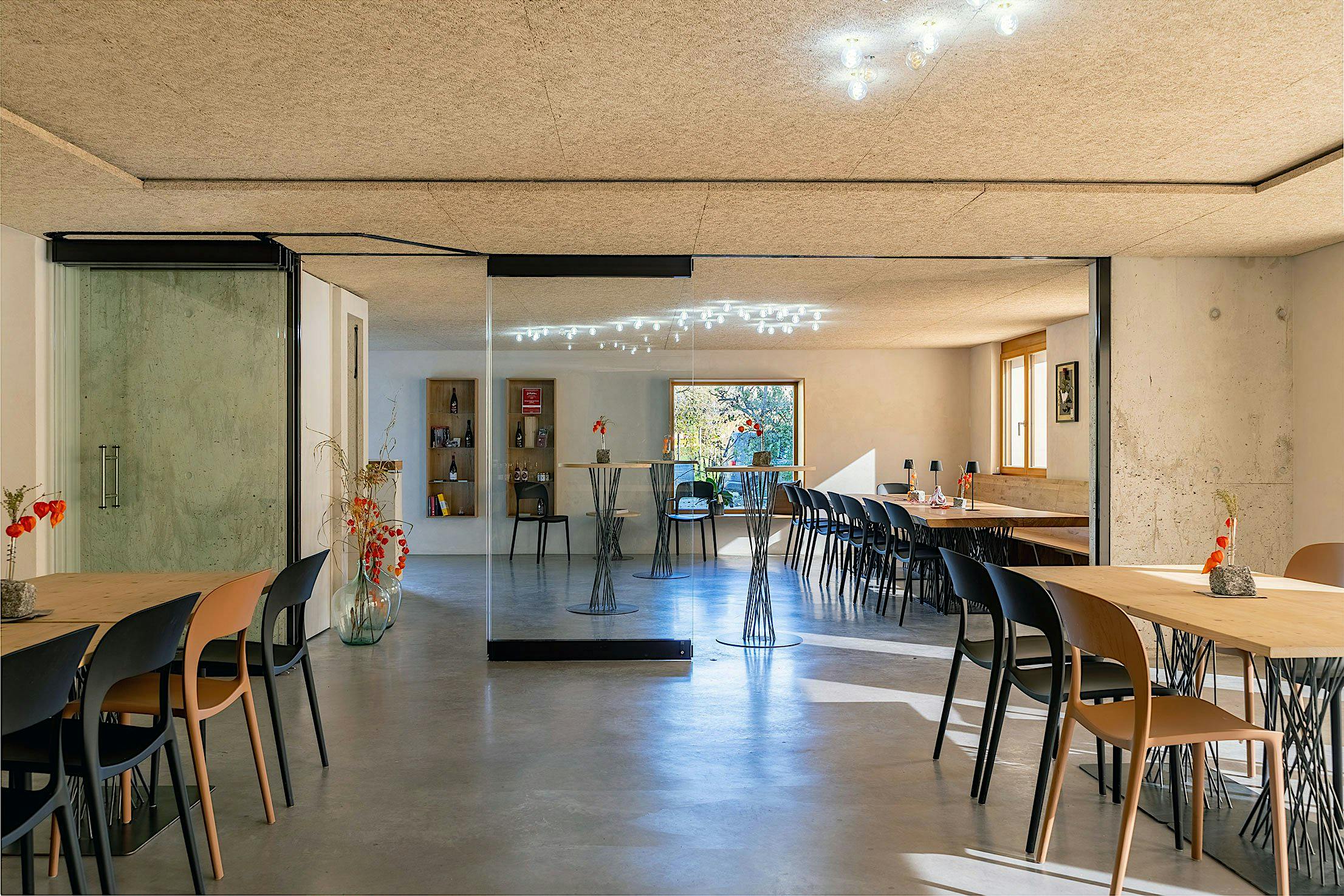 A modern wine tasting room with long tables and chairs, sliding glass doors in the background, and decorative lighting.
