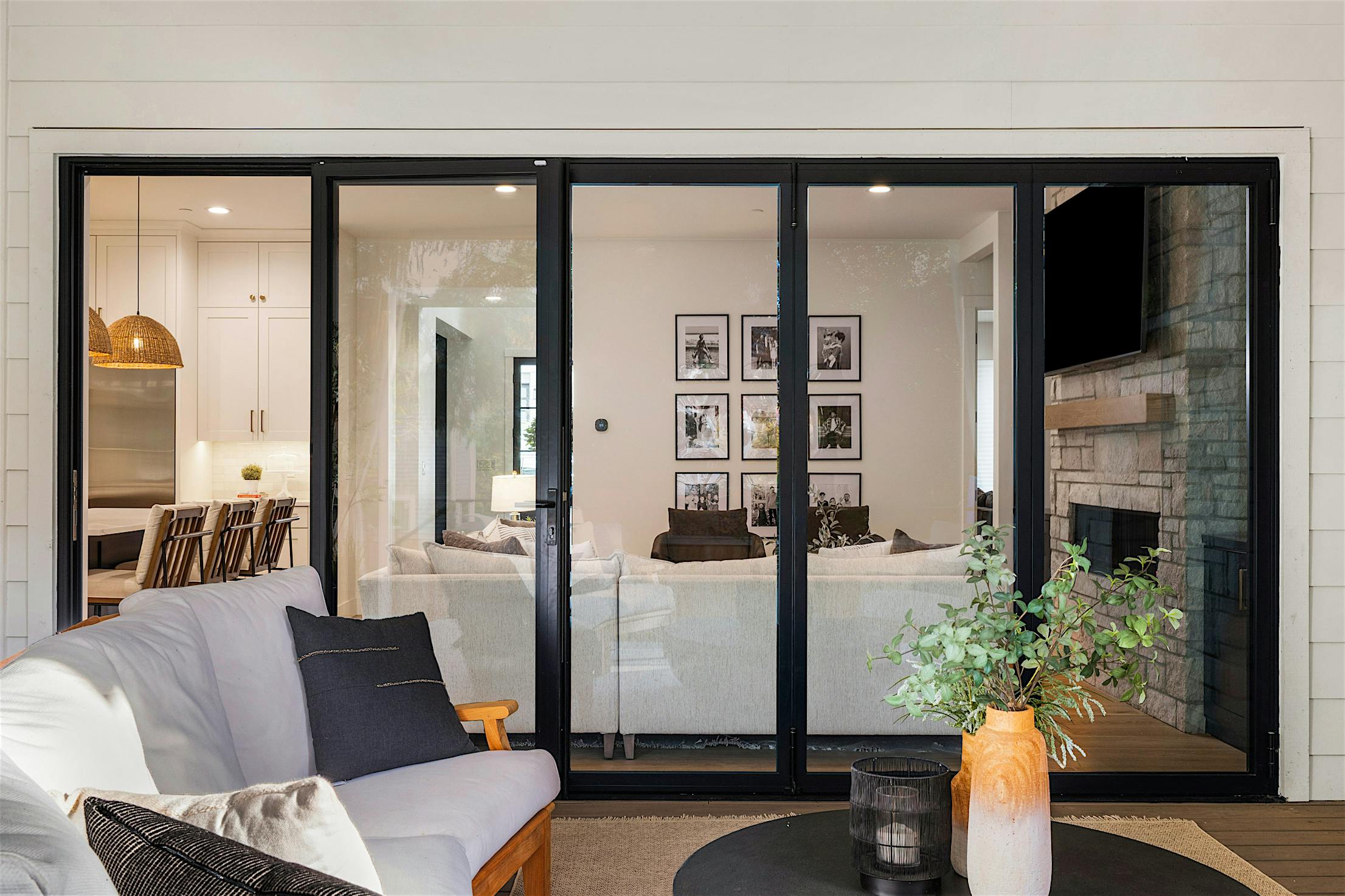Peering through bifold glass doors, find a modern living room with white couches, framed pictures on the wall.