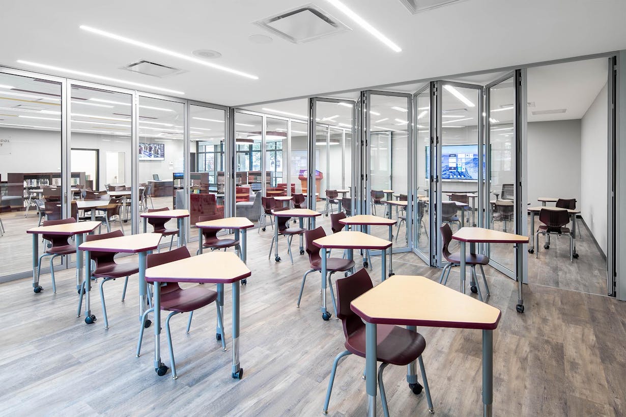 A classroom with tables and chairs and glass walls comprised of acoustical folding glass walls