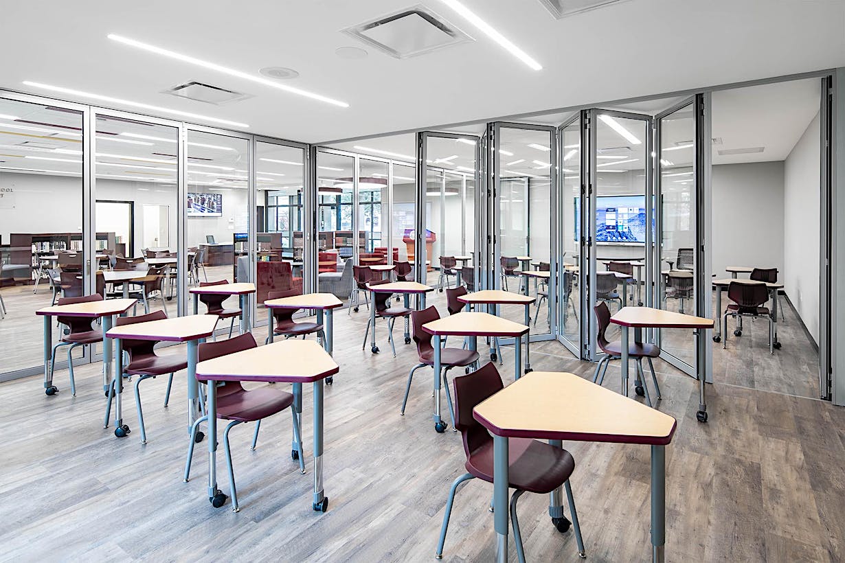 A classroom with tables and chairs and glass walls comprised of acoustical folding glass walls