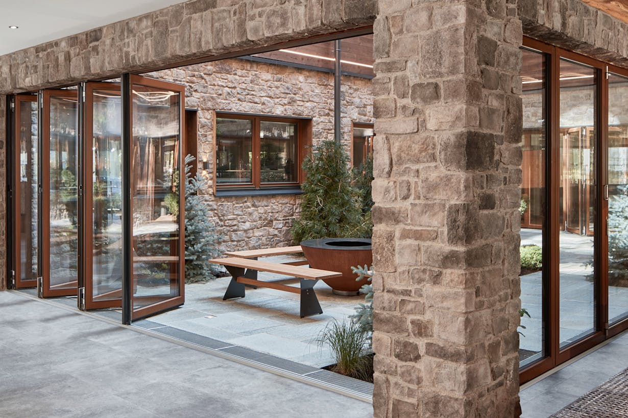 A living room with stone walls and wood framed folding glass walls