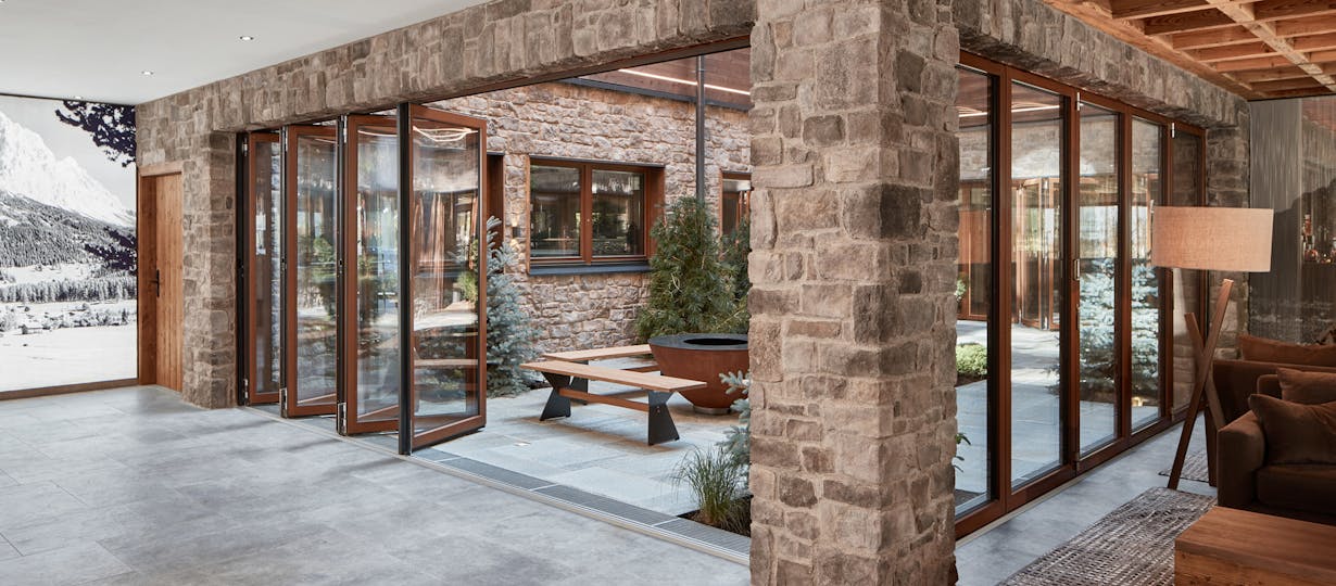 A living room with stone walls and wood framed folding glass walls