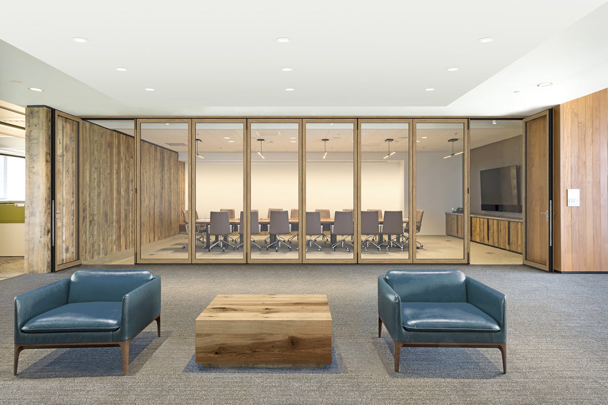 A conference room with acoustical glass walls with two blue chairs and a table