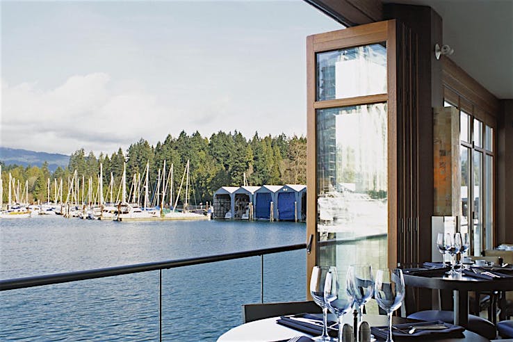 Restaurant dining area with set tables overlooks a marina with botas through large wood framed accordion glass doors.