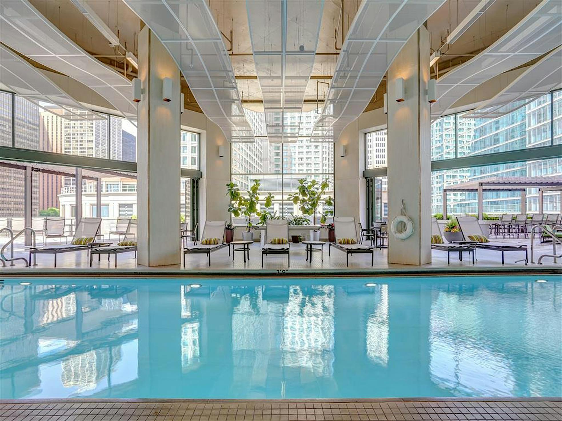 Indoor pool with lounge chairs, city views, and opening glass doors for fresh air and easy access.