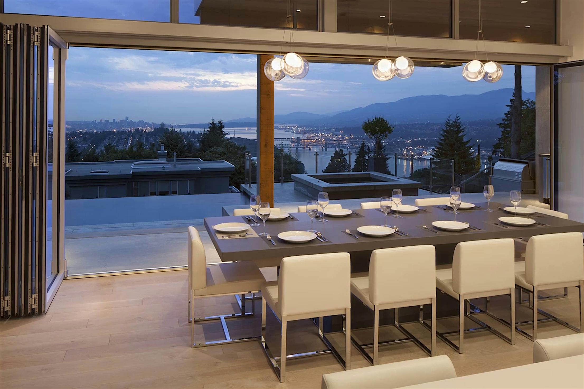 Modern dining room with intelligent rollers on folding glass doors, a table for eight, and scenic city-mountain views at dusk.